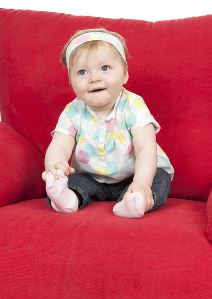Bebê menina sentada em um grande sofá vermelho . — Fotografia de Stock