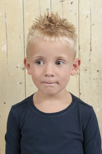 Little boy standing against an old wooden door — Stock Photo, Image