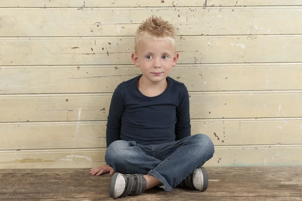 Mały chłopiec siedzi przed stare drewniane drzwi — Zdjęcie stockowe