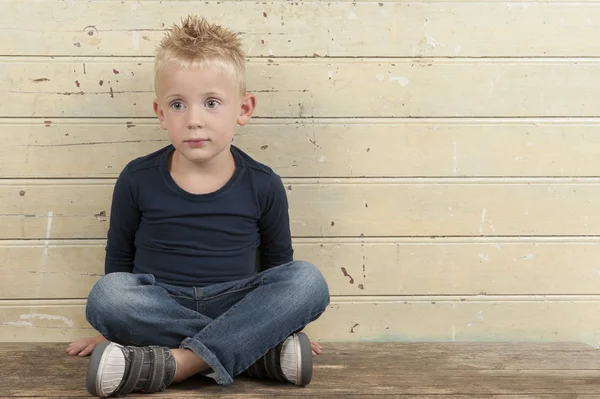 Liten pojke sitter mot en gammal trä dörr — Stockfoto