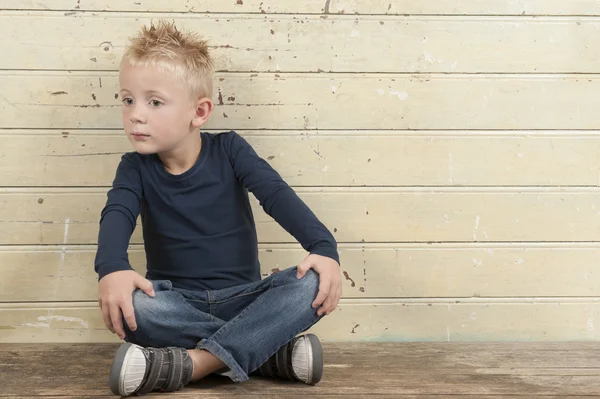 Nyfiken liten pojke sitter mot en gammal trä dörr — Stockfoto