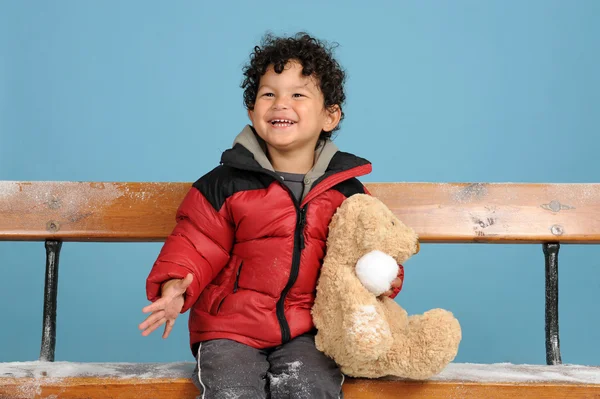 Pequeno menino wit ursinho sentado em um banco — Fotografia de Stock