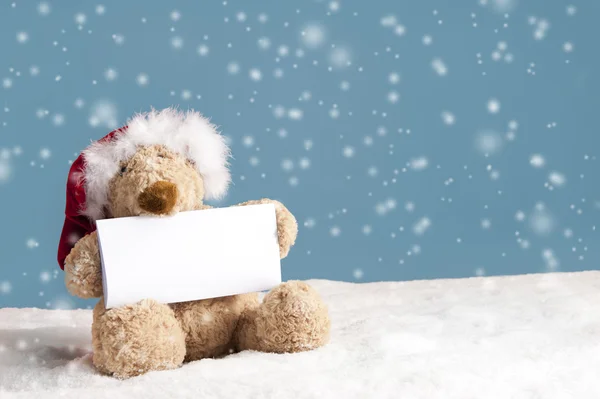 Ours en peluche avec chapeau de Noël et carte de message assis dans la neige — Photo