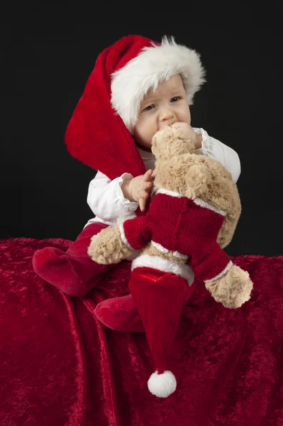 Pequeño bebé con sombrero de Navidad, sentado en una almohada roja — Foto de Stock