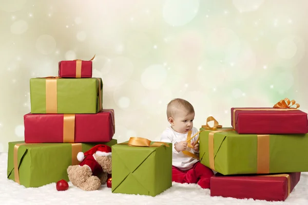 Baby sitzend zwischen Weihnachtsgeschenken, Bokeh-Hintergrund — Stockfoto