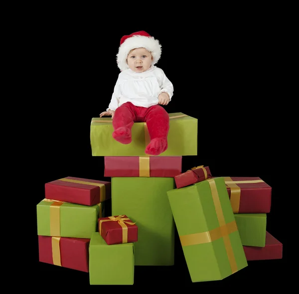 Baby sitzt auf einem Stapel Weihnachtsgeschenke, schwarzer Hintergrund — Stockfoto