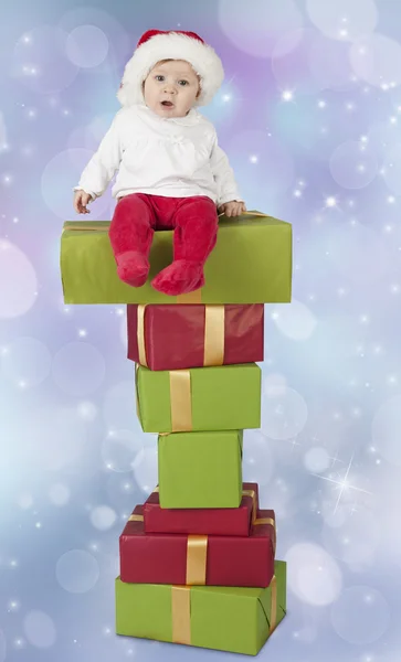 Baby seated on a stack of christmas presents, bokeh background — Stock Photo, Image