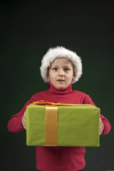 Junge mit Weihnachtsmütze und Geschenk auf dunkelgrün — Stockfoto