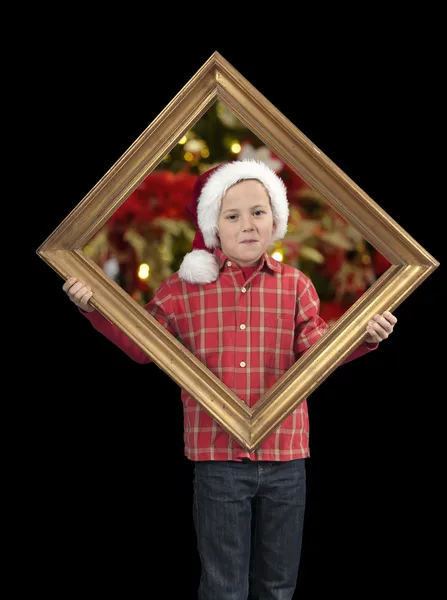 Garçon avec chapeau de Noël tenant un cadre doré, sur noir — Photo