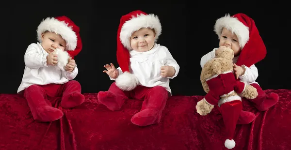 Drie kleine baby's met kerst hoed, zittend op een rode kussen Rechtenvrije Stockafbeeldingen