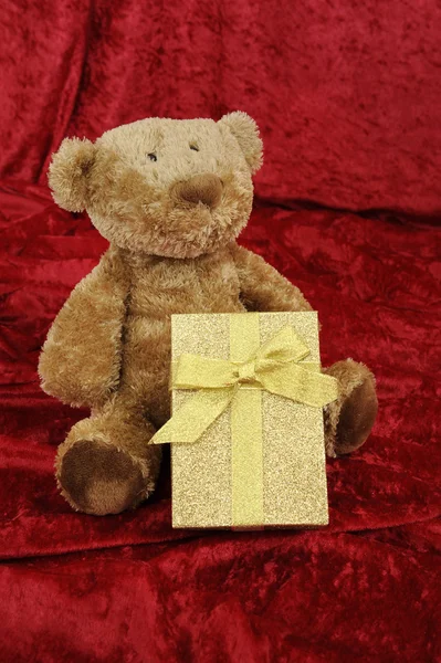 Teddybeer met golden cadeau doos op rood — Stockfoto