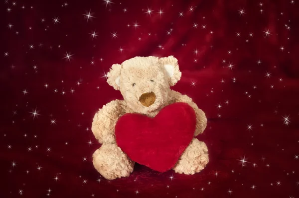 Teddybeer met hartvormige kussen op rood — Stockfoto