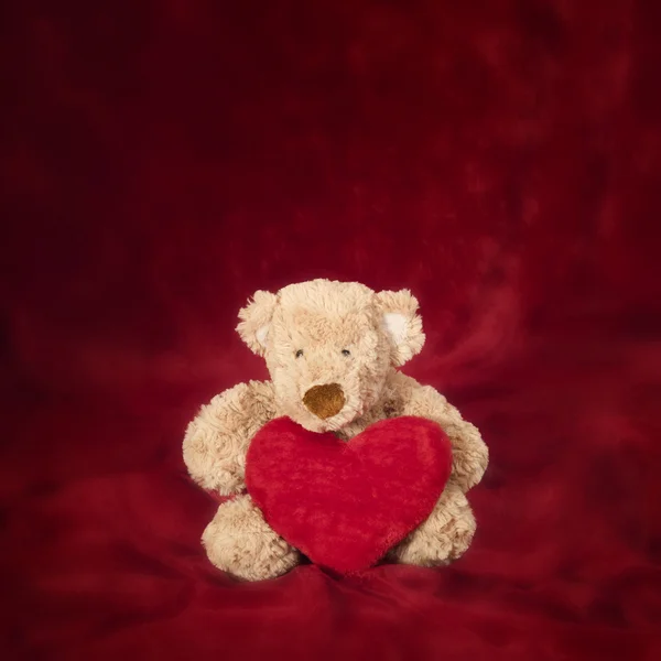 Urso de pelúcia com travesseiro em forma de coração no vermelho — Fotografia de Stock