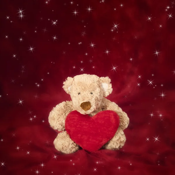 Teddybär mit herzförmigem Kissen auf rot — Stockfoto