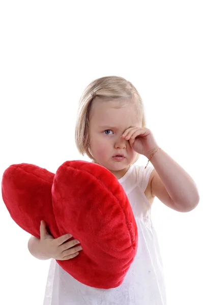 Küçük kızla yorgun gözlerini ovuşturarak kırmızı kalp şeklinde yastık — Stok fotoğraf