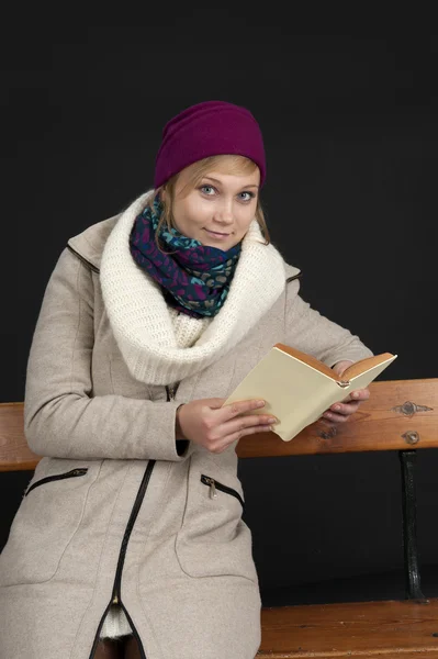 Young woman in winter clothes reading on a bench — Stock Photo, Image