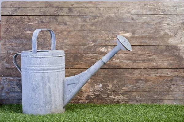 Watering can on grass against a wooden wall — Stock Photo, Image