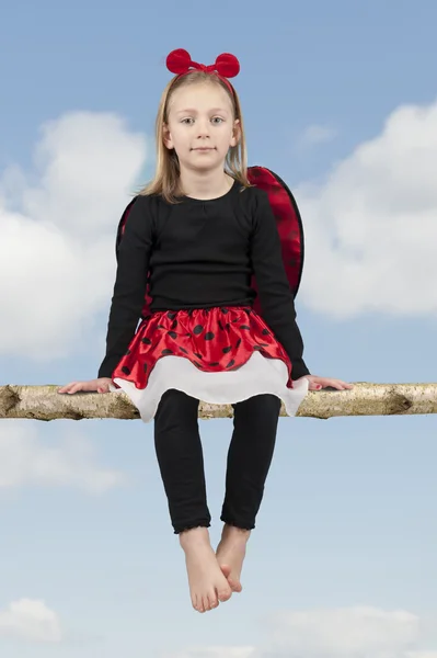 Little girl in lady bug costume seated on a branch — Stock Photo, Image