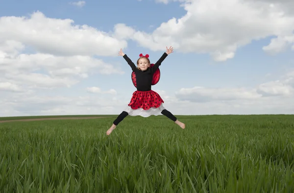 Little girl in lady bug costume jumping in the fileds — Stock Photo, Image