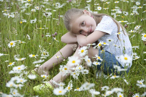 Girl seated in meadow between daisies — Stock Photo, Image