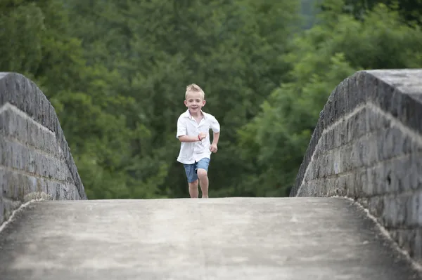 Summer time : little boy running on a bridge — Stock Photo, Image