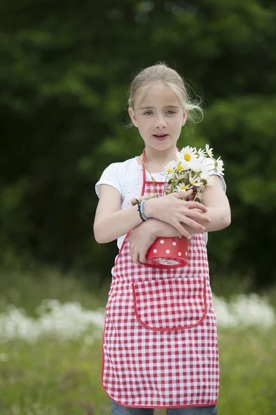 Dívka zástěry a kyticí sedmikrásek venku — Stock fotografie