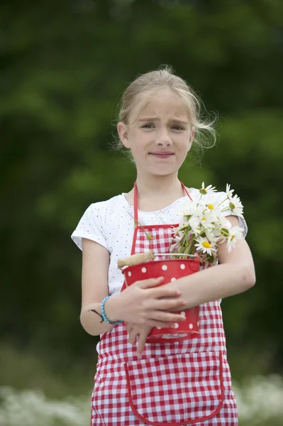 Dívka zástěry a kyticí sedmikrásek venku — Stock fotografie