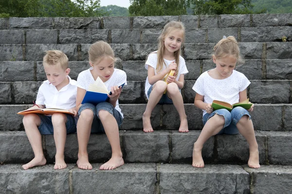 Summer holidays: children with a book seated outdoors on stairs — Stock Photo, Image