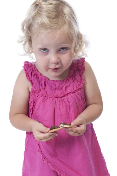 Маленькая девочка в розовом ест печенье, изолированное на белом — стоковое фото
