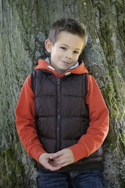 Shy young boy leaning against a tree — Stock Photo, Image