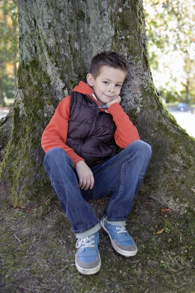 Pojken sitter mot ett träd — Stockfoto