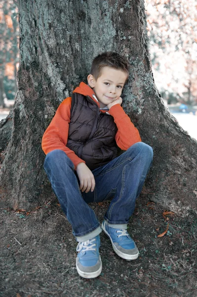 Niño sentado contra un árbol Fotos De Stock