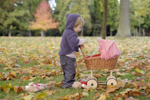 Liten flicka spelar med barnvagn i parken — Stockfoto