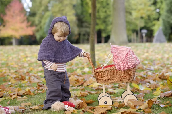 Little girl playing with a pram in the park — Stock Photo, Image