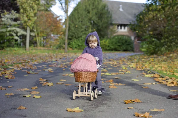 Little girl playing with a pram in a park — Stock Photo, Image