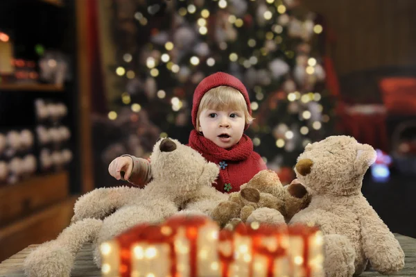 Piccolo bambino con un sacco di orsacchiotti di peluche davanti a un albero di Natale — Foto Stock