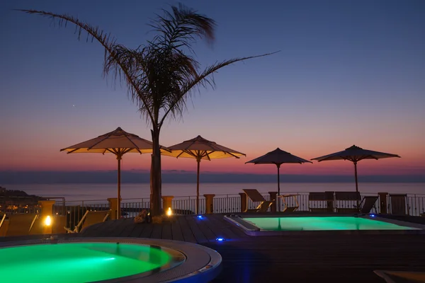 Hora de verano: hermoso amanecer en la zona de la piscina con palmeras y sombrillas , — Foto de Stock