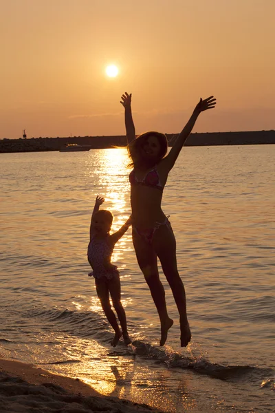 Lady and little girl jumping on the beach enjoying summer — Stock Photo, Image