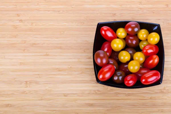 Сherry tomatoes in black plate on wooden table with slices of g — Stock Photo, Image
