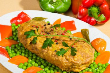 Maydanoz, bezelye ve havuçla süslenmiş bir tabak doldurulmuş etle dolu bir masa..