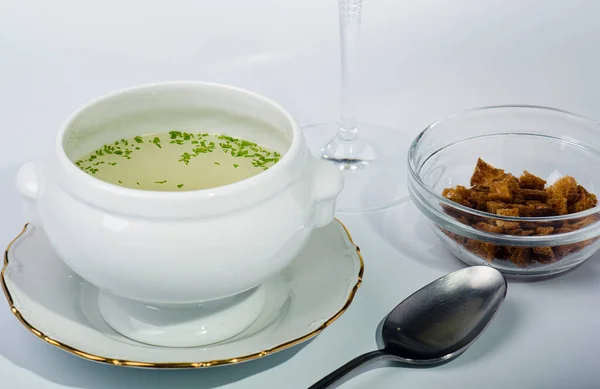 Ceramic soup tureen with clear soup, accompanied by a plate of toasted bread.