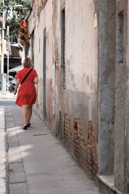 BARCELONA, SPAIN - 29 Haziran 2021: Kırmızı elbiseli bir kadın kırmızı ışık açık bir trafik ışığına doğru yürüyor.