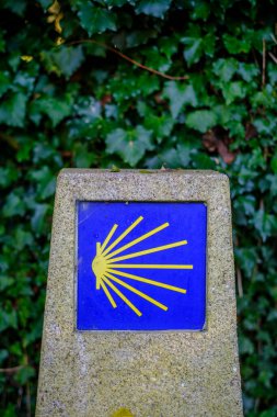 Granite post with the yellow icon on a blue background, indicating the Camino de Santiago in Galicia (Spain)