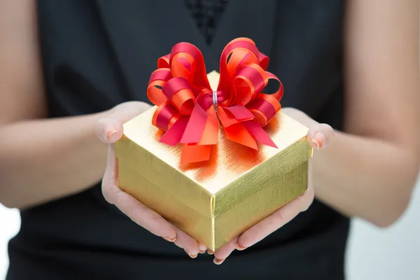 Caja de regalo de oro con lazo de satén rojo y naranja en la mano — Foto de Stock