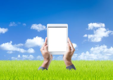 adam el dijital tablet yeşil çim ve mavi gökyüzü arka plan üzerinde tutarak
