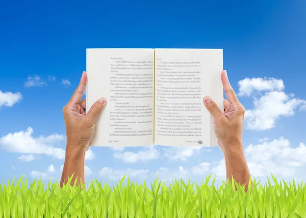 Man händer som håller boken på gröna fält med blå himmel bakgrund — Stockfoto