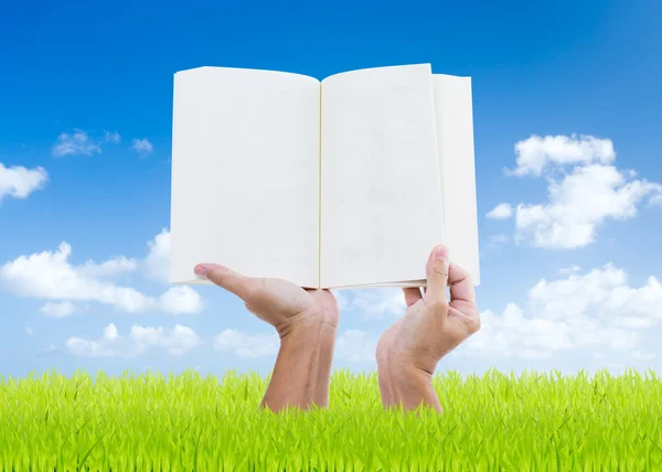 Las manos del hombre sosteniendo el libro en el campo verde con fondo azul cielo — Foto de Stock