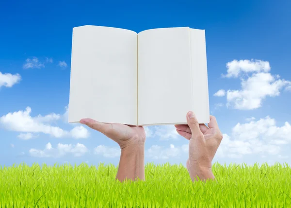 Uomo mani tenendo libro su campo verde con sfondo cielo blu — Foto Stock