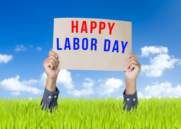 Happy labor day cardboard with man hand over green field and blue sky background