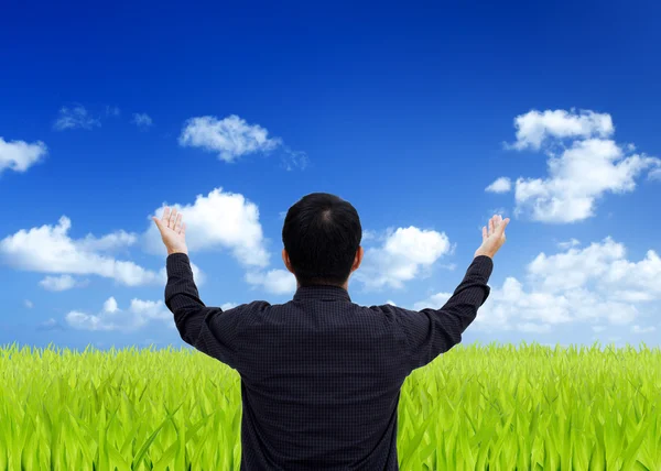 Man stretching out his hand on a green field with blue sky — Stock Photo, Image